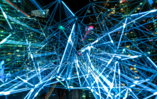 Nachtszene einer Großstadt mit blau leuchtendem Netzwerk aus Linien und Knotenpunkten – Symbol für KI, Datenströme und digitale Vernetzung.