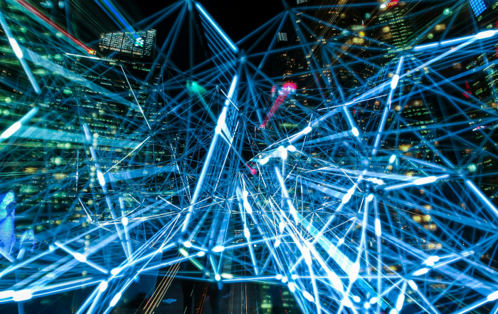 Nachtszene einer Großstadt mit blau leuchtendem Netzwerk aus Linien und Knotenpunkten – Symbol für KI, Datenströme und digitale Vernetzung.