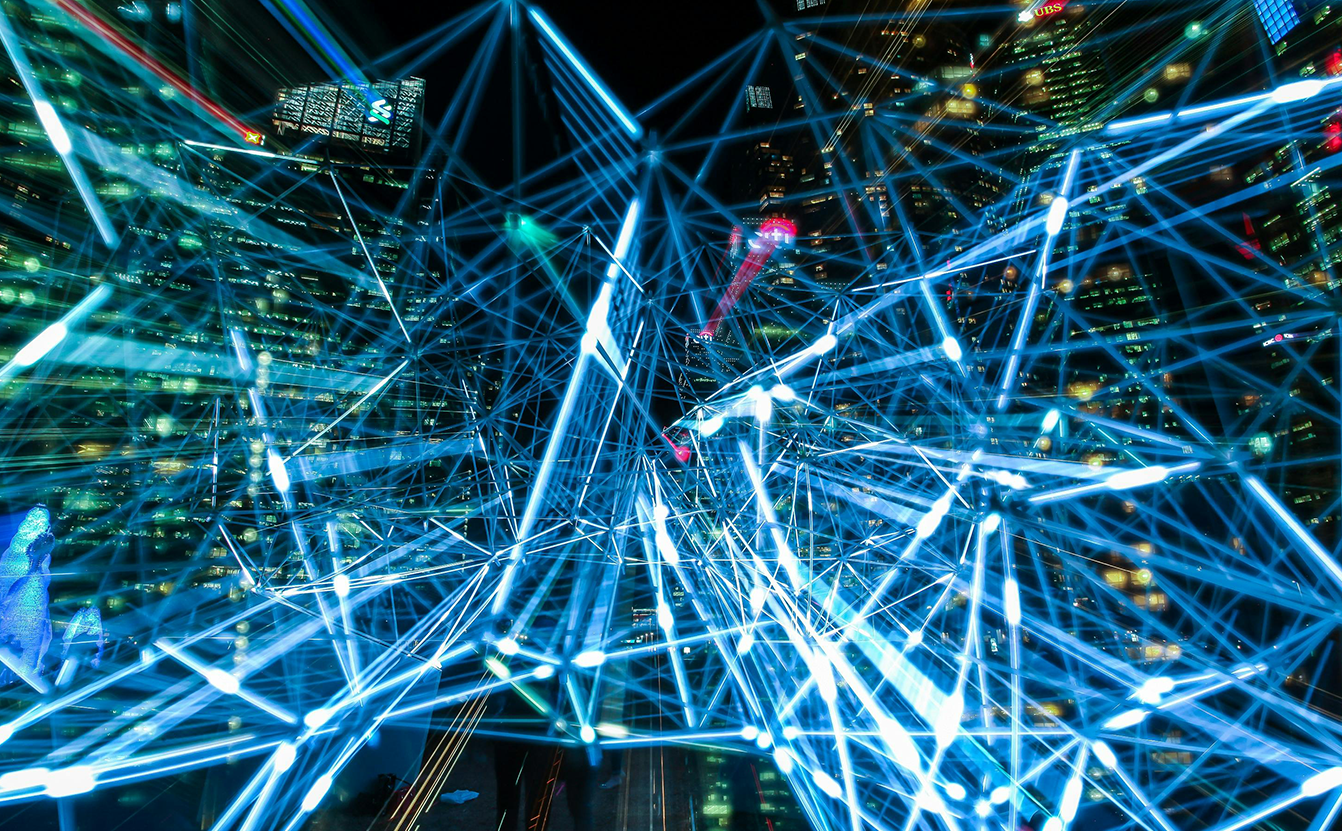 Nachtszene einer Großstadt mit blau leuchtendem Netzwerk aus Linien und Knotenpunkten – Symbol für KI, Datenströme und digitale Vernetzung.